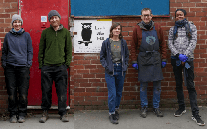 Our team of 6 outside our workshop photographed in front of the brick walls of the building. Our red front door and sign are in the photo.